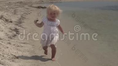美丽的小女孩沿着海岸奔跑。笑宝贝。穿着白色连衣裙的小女孩在海边跑步。慢动作。